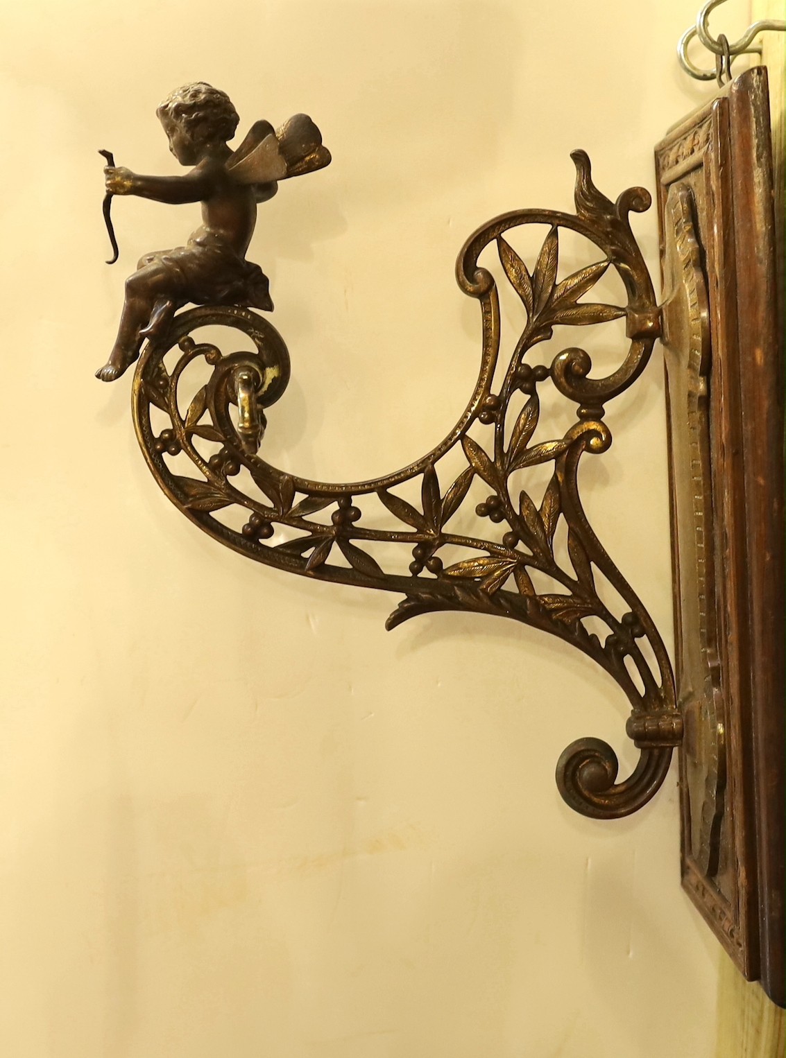 A late Victorian aesthetic movement ormolu wall bracket, modelled with Cupid and laurel leaves, mounted on an oak wallplate, height 34cm. depth 25cm